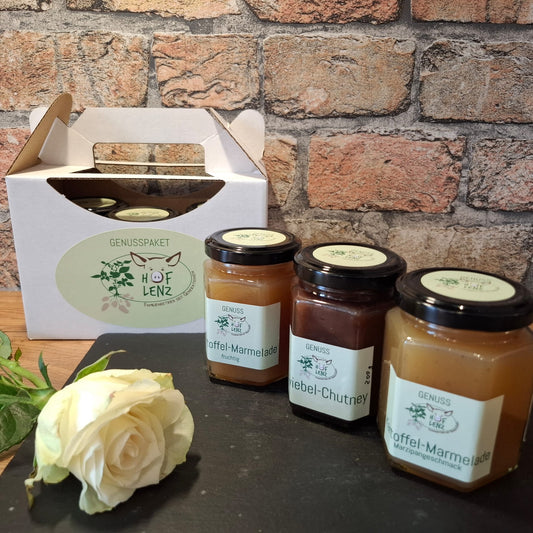 Genusspaket vom Hof Lenz mit Kartoffel-Marmelade fruchtig, Zwiebel-Chutney und Kartoffel-Marmelade Marzipangeschmack in Geschenkbox vor Backsteinwand.